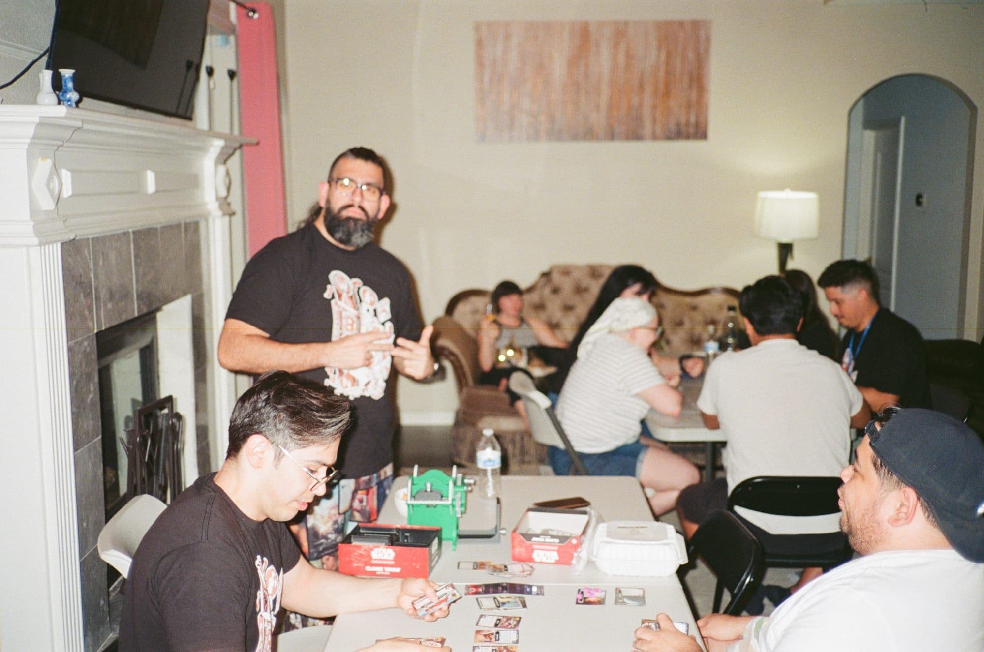 A living room full of people playing games at folding tables late at night