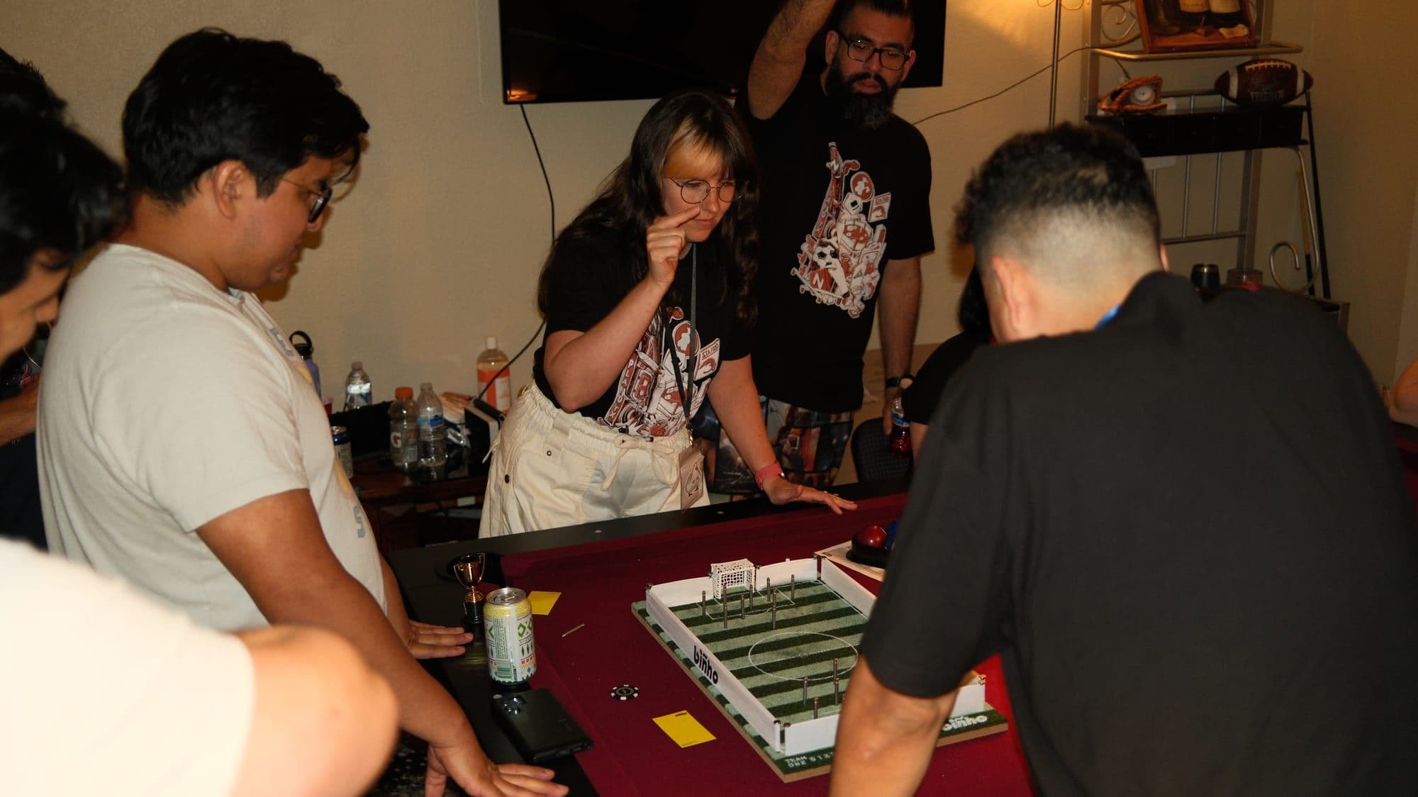 Players crowded around a table, leaning in over a Biñho board mid game