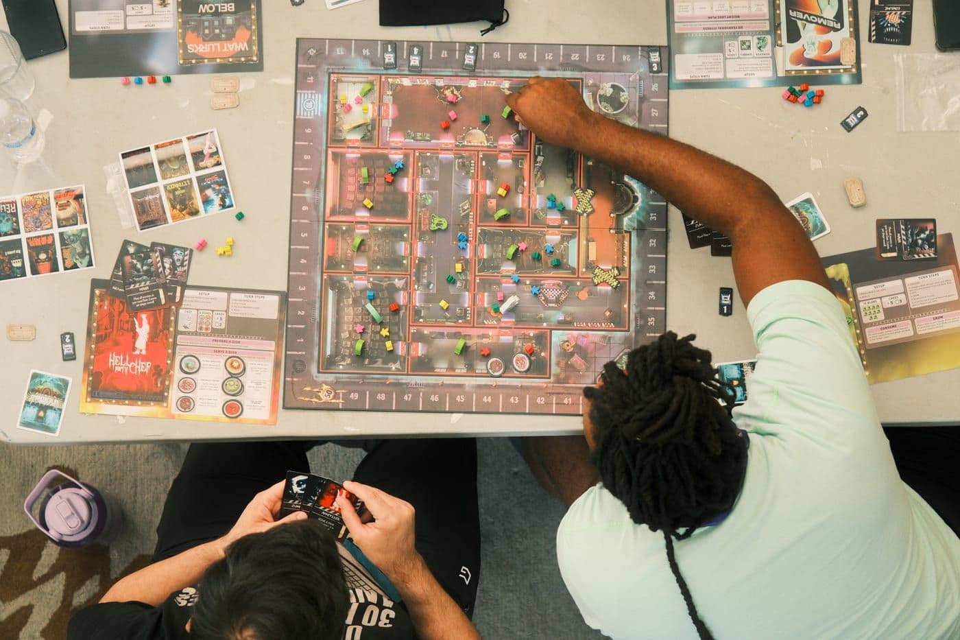 Overhead view of two players mid game, board covered in coloured pieces