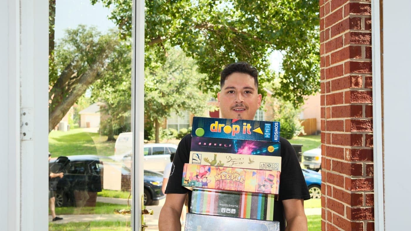A winner in a doorway carrying a tall stack of board game boxes